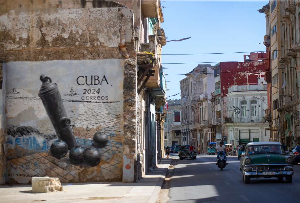 AME8987. LA HABANA (CUBA), 19/11/2024.- Un carro pasa frente a un graffiti en la calle San Lázaro, este martes en La Habana (Cuba). Las calles del centro histórico de la capital de Cuba se han convertido estos días en parte del escenario de la Bienal de La Habana, una de las principales citas culturales del país, donde cerca de 400 artistas, 230 de ellos extranjeros, exponen sus obras en una mirada de exposiciones, actuaciones y performances que arrancaron este noviembre y se prolonga hasta finales de febrero. EFE/Yander Zamora