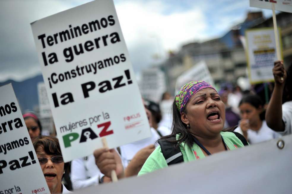 Una mujer afro en medio de una marcha sostiene un cartel que dice terminemos la guerra, construyamos la paz.