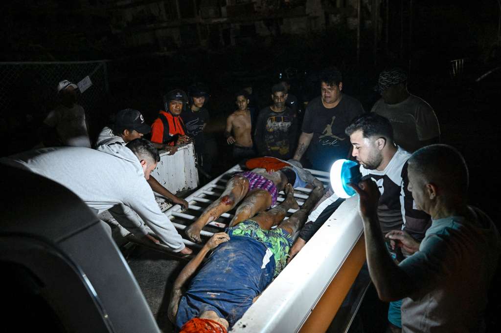 Unas personas cargan dos cuerpos tras unos terremotos en Venezuela que causaron graves estragos en La Guaira.