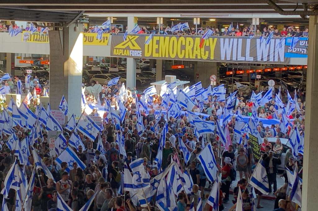 TEL AVIV (ISRAEL), 11/07/2023.- Con un bullicio ensordecedor, las multitudinarias protestas en Israel contra la reforma judicial del Gobierno volvieron este martes al aeropuerto internacional de Tel Aviv, donde la Policía se enfrentó cuerpo a cuerpo con la marea de manifestantes mientras los pasajeros se abrían paso entre el caos. Entre banderas israelíes, tambores y estridentes cornetas, unas 7.000 personas tomaron la entrada principal de la terminal aérea al grito de "!democracia!". Levantando el puño y pancartas contra el Gobierno de Benjamín Netanyahu -el más derechista de la historia de Israel-, los manifestantes bloquearon los carriles por donde normalmente pasan taxis y autobuses para recoger a los pasajeros. EFE/ Yemeli Ortega