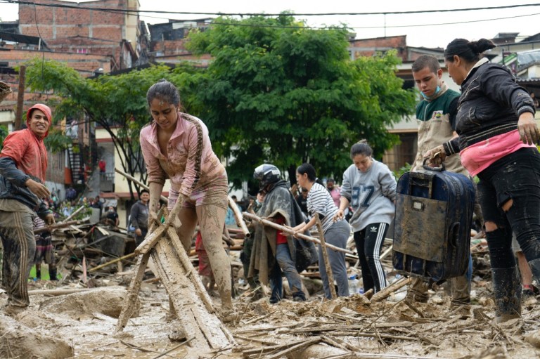 Una mujer ayuda a levantar unas tablas entre el lodo