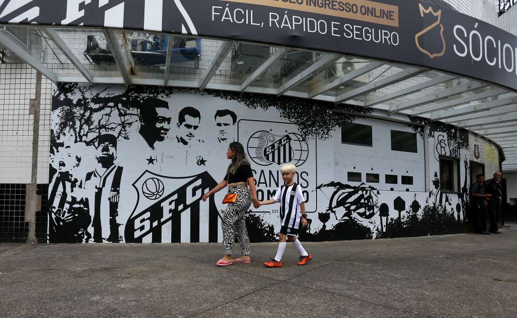 AME3199. SANTOS (BRASIL), 29/12/2022.- Una mujer y un niño caminan frente a un mural del Club Santos en el estadio Urbano Caldeira en la Vila Belmiro, tras conocerse la noticia de la muerte de la leyenda del fútbol brasileño Pelé, hoy, en la ciudad de Santos (Brasil). Los clubes brasileños de primera división sin excepción rindieron este jueves homenajes al tricampeón mundial Edson Arantes do Nascimento 'Pelé', que murió a sus 82 años y al que se refirieron como el "eterno" rey del fútbol. Como "Eterno" lo despidió el Santos, el club en que Pelé se inmortalizó y en que jugó casi toda su carrera. EFE/ Guilherme Dionizio