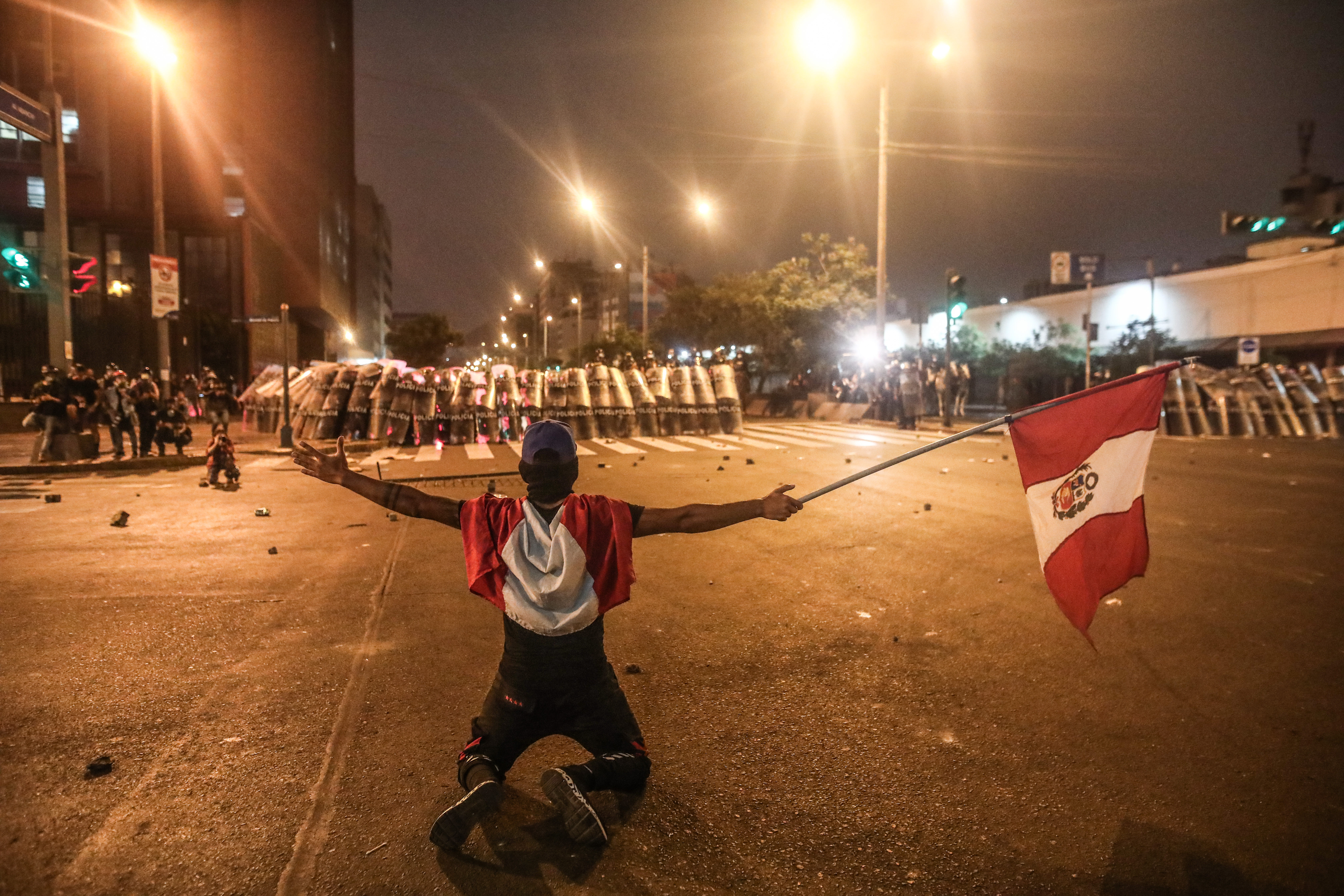 LIMA (PERÚ), 05/04/2022.- Un manifestante ondea una bandera frente a un cerco policial hoy, en Lima (Perú). Miles de peruanos desafiaron este martes el toque de queda ordenado por el presidente Pedro Castillo para Lima y su vecina provincia de Callao y se manifestaron en la capital para pedir la renuncia del mandatario. EFE/ Aldair Mejía