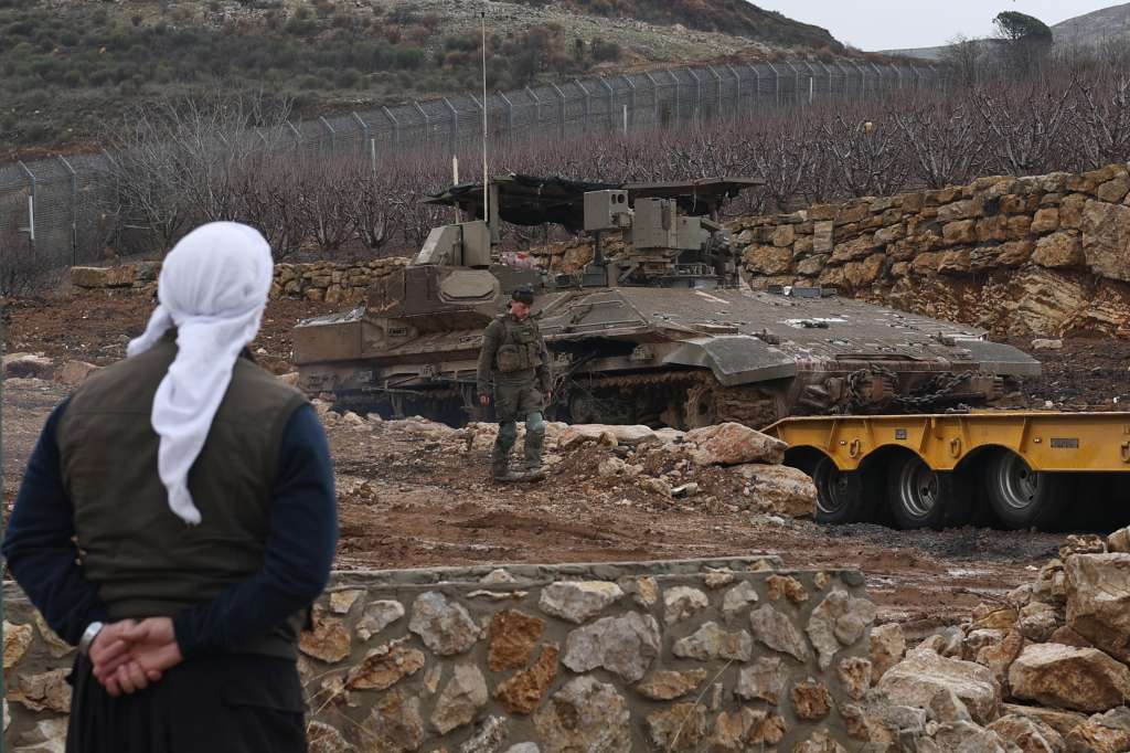 FOTODELDÍA Majdal Shams (Siria), 26/12/2024. - Un druso observa un soldado israelí y un vehículo blindado de transporte de tropas (APC) en un camión mientras los soldados salen de la zona de amortiguación, en la frontera entre Israel y Siria, cerca de la aldea drusa de Majdal Shams, en los Altos del Golán anexionados por Israel,este jueves. El ejército de Israel dijo que las fuerzas de los paracaidistas, junto con otras tropas, están llevando a cabo 'actividades de defensa' para prevenir 'cualquier amenaza' y se despliegan en posiciones clave dentro de la zona de amortiguación.EFE/ Atef Safadi