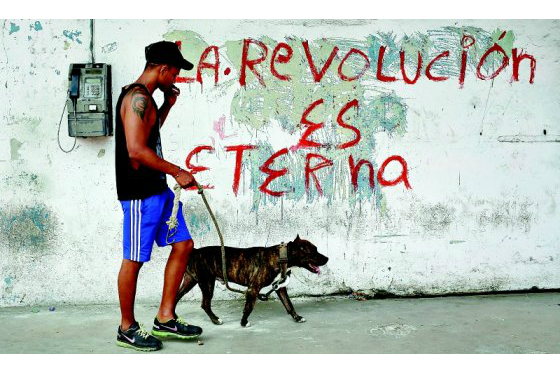 Un joven pasea con su perro junto a un cartel alusivo a la Revolución Cubana en una calle de La Habana (Cuba). / EFE