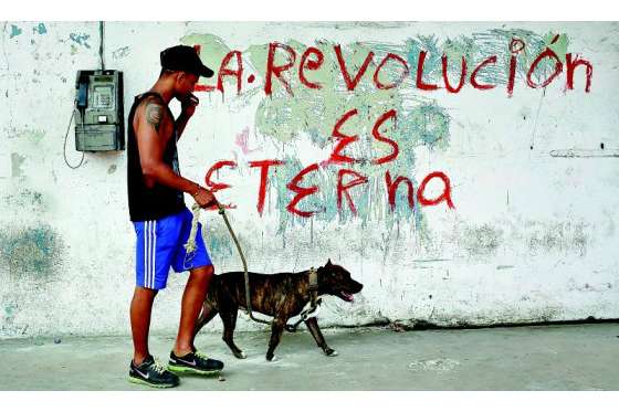 Un joven pasea con su perro junto a un cartel alusivo a la Revolución Cubana en una calle de La Habana (Cuba). / EFE
