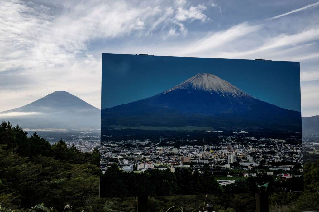 A sign with a photo of Mount Fuji covered in snow is seen at a view point as Mount Fuji, the highest mountain in Japan at 3,776 metres, looms in the background in Gotemba, Shizuoka prefecture on October 31, 2024.