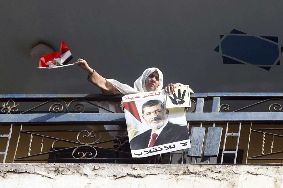Una simpatizante del depuesto presidente egipcio Mohamed Mursi ondea una bandera mientras asoma por un balcón una fotografía suya, durante una protesta en El Cairo (Egipto). / EFE