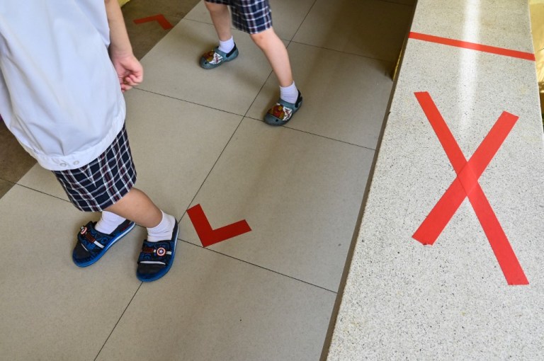 Dos estudiantes están de pie junto a los marcadores de distanciamiento social que están usando las escuelas para evitar la propagación del nuevo coronavirus COVID-19