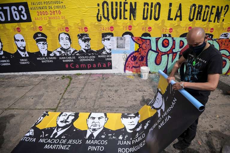 Hombre enrolla un cartel donde están las caras de militares investigados por falsos positivos.