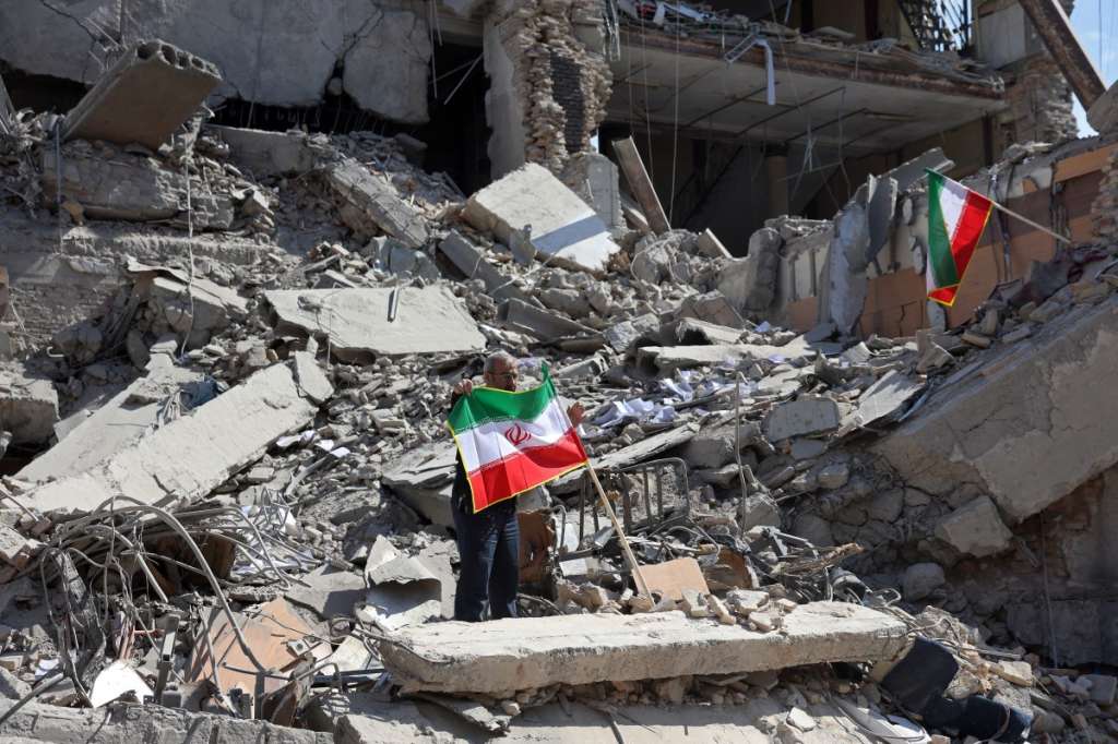 A man holds an Iranian flag amid the debris of a destroyed building following airstrikes in central Tehran on March 4, 2026. Iran's Revolutionary Guards said on March 4 they had total control of the Strait of Hormuz, a key waterway for global energy transit, as Israel launched a new wave of strikes on the Iranian capital. (Photo by AFP)