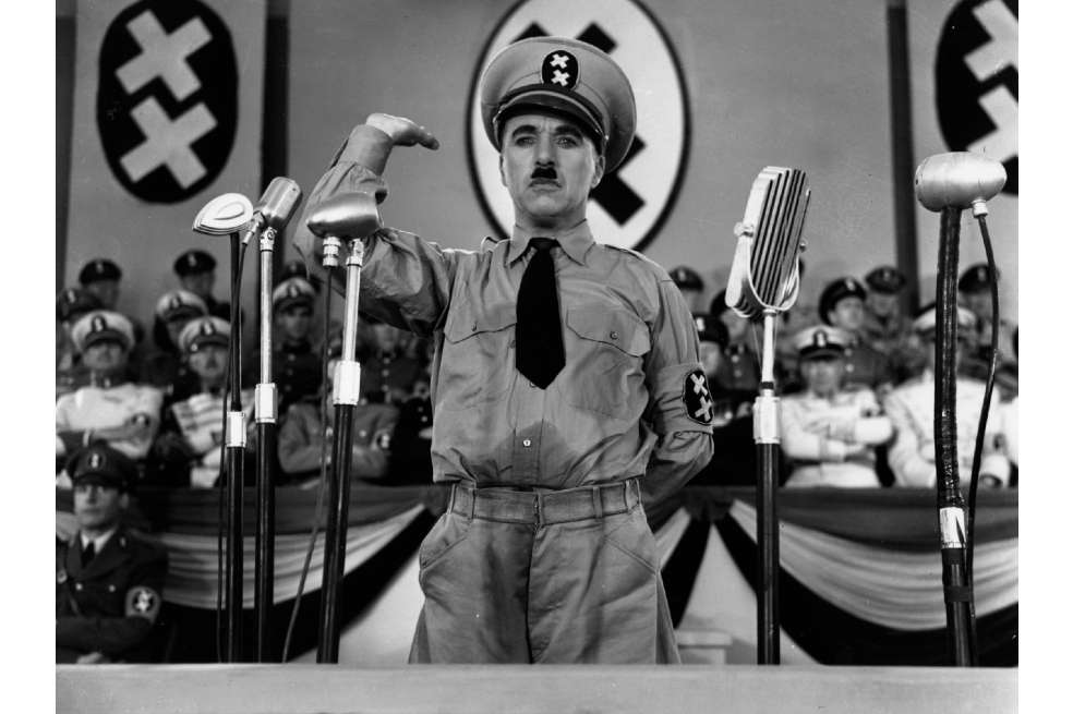 Charles Chaplin interpretando el papel de "El Gran Dictador". El personaje tiene la mano derecha levantada y parece dando un discurso.