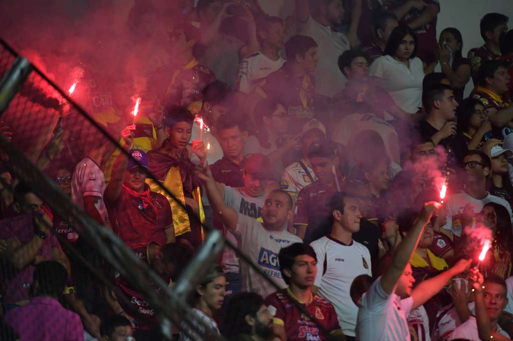 Hinchas del Tolima con bengalas y banderas en un gradería.