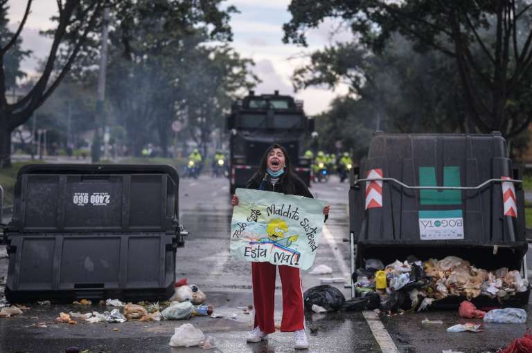 Una mujer gritando al frente de una tanqueta del Esmad y al lado de dos contenedores de basura derribados