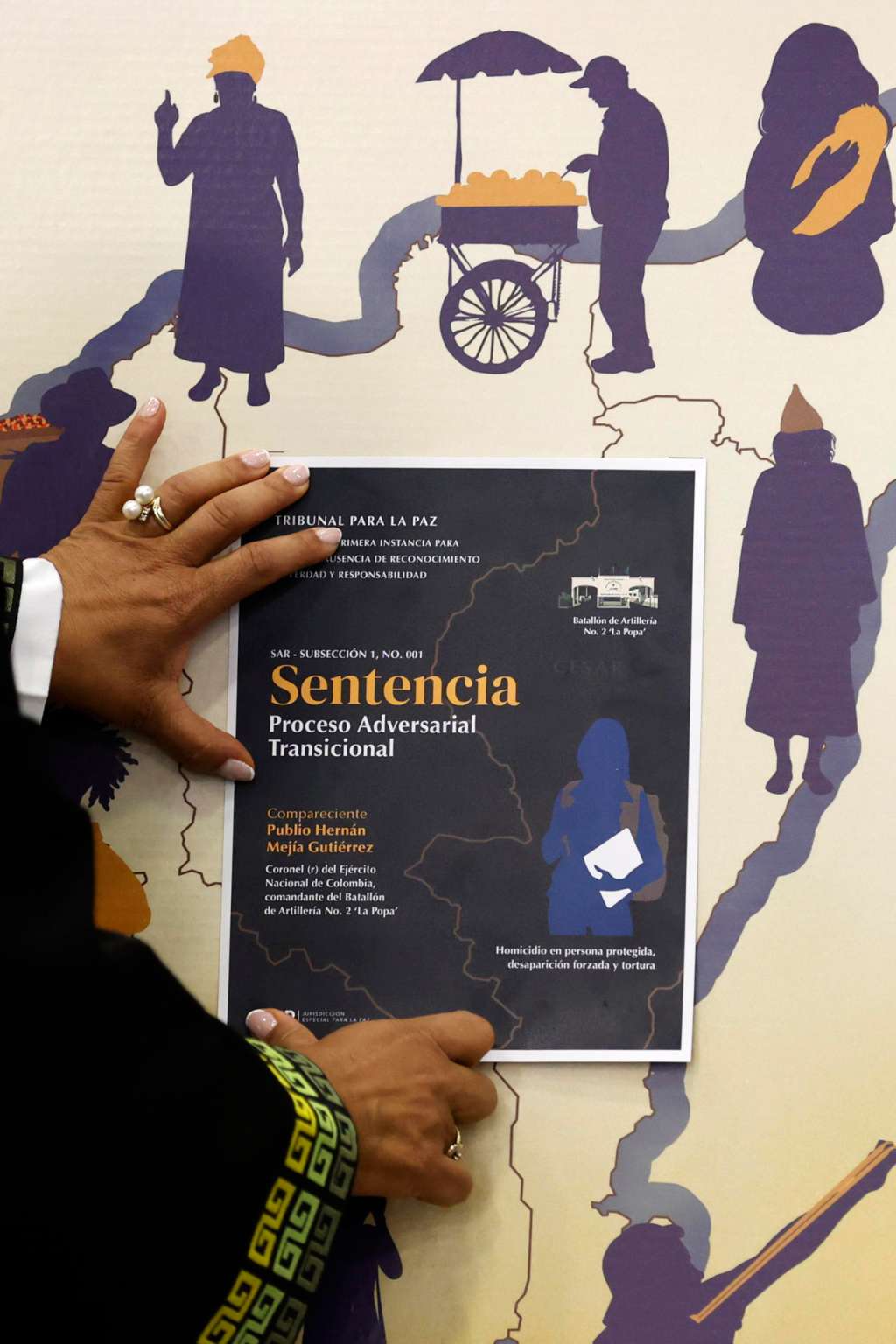 AME9578. BOGOTÁ (COLOMBIA), 19/12/2025.- La magistrada de la sección de ausencia de reconocimiento de verdad y responsabilidad de la JEP, Reinere Jaramillo Chaverra, ubica la imagen de la sentencia en un mapa donde ocurrieron los hechos violentos durante el anuncio de la Primera Sentencia Adversarial Transicional en el proceso del coronel (r) Publio Hernán Mejía Gutiérrez, este viernes en Bogotá (Colombia). La Jurisdicción Especial para la Paz (JEP) condenó a 20 años de prisión a Hernán Mejía al hallarlo penalmente responsable de crímenes de guerra y de lesa humanidad por 72 asesinatos y desapariciones forzadas de civiles presentados como bajas en combate en el norte del país. EFE/ Mauricio Dueñas Castañeda