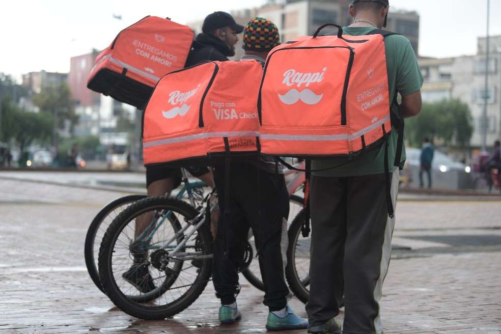 Tres domiciliarios conversan en la calle junto a sus bicicletas.