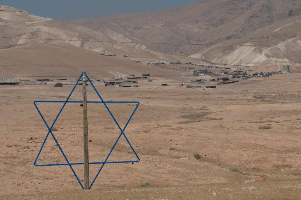 RAS EIN AL AUYA/MURRAYAT(CISJORDANIA), 08/06/2025.- Estrella de David o Escudo de David en Cisjordania ocupada y de fondo comunidades beduinas del Valle del Jordán. Según el derecho internacional, toda forma de asentamiento en territorios conquistados mediante ocupación militar, como es el caso de Cisjordania, ocupada por Israel desde 1967, constituye una violación grave. No obstante, dentro del marco legal israelí, la mayoría de las colonias ya existentes han sido regularizadas. EFE/Magda Gibelli