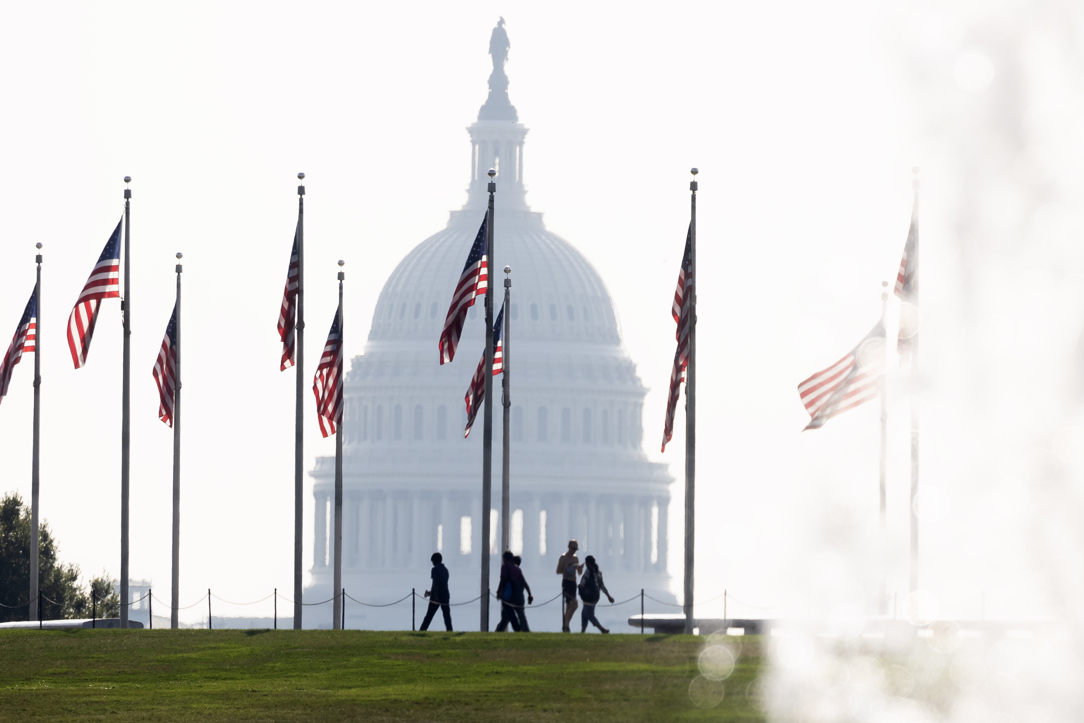 Washington (United States), 28/07/2023.- Visitors to the base of the Washington Monument walk beneath US national flags, with the US Capitol seen behind and a fountain from the World War II Memorial in front, during a heat advisory in Washington, DC, USA, 28 July 2023. An excessive heat warning has been issued for the US capital area, with a heat index forecast to reach 110 F (43.3 C) on 28 July and 108 F (42.2 C) on 29 July. EFE/EPA/MICHAEL REYNOLDS