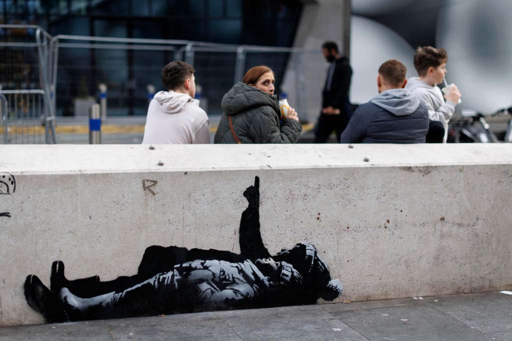 LONDON (United Kingdom), 22/12/2025.- People sit behind a new street artwork near the Centre Point building, on the intersection of Tottenham Court Road and Oxford Street, in central London, Britain, 22 December 2025. The piece has prompted speculation that British street artist Banksy may be behind the artwork. (Reino Unido, Londres) EFE/EPA/TOLGA AKMEN