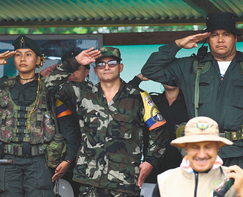 FARC EP dissidence top commander, aka Ivan Mordisco (C), gives a military salute next to commander Calarca (R) during a meeting with local communities in San Vicente del Caguan, Caqueta department, Colombia, on April 16, 2023. An armed dissident group of Colombia's disbanded FARC guerrillas said Sunday it was "ready" to start peace talks with the government from May 16. "We are announcing to the world that our delegates to the dialogue table with the Colombian government... are ready for May 16," the EMC dissident grouping, which rejected a 2016 peace deal that disarmed the FARC, said through a spokesperson. (Photo by JOAQUIN SARMIENTO / AFP)