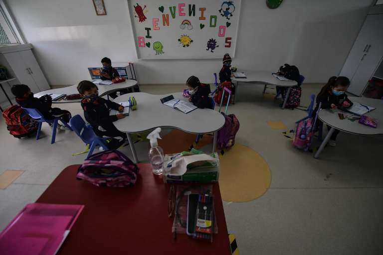 Niños con tapabocas sentados en pupitres.