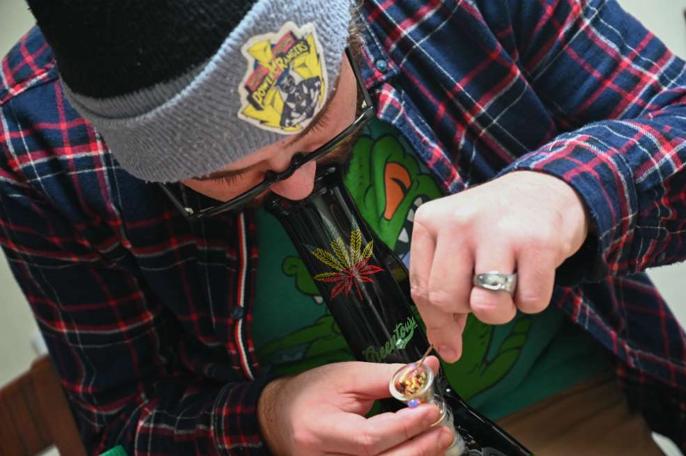 Un miembro del tour de cannabis se prepara para fumar en un bong en medio de una parada del grupo que participa en el recorrido ofrecido por Green Tours. / AFP