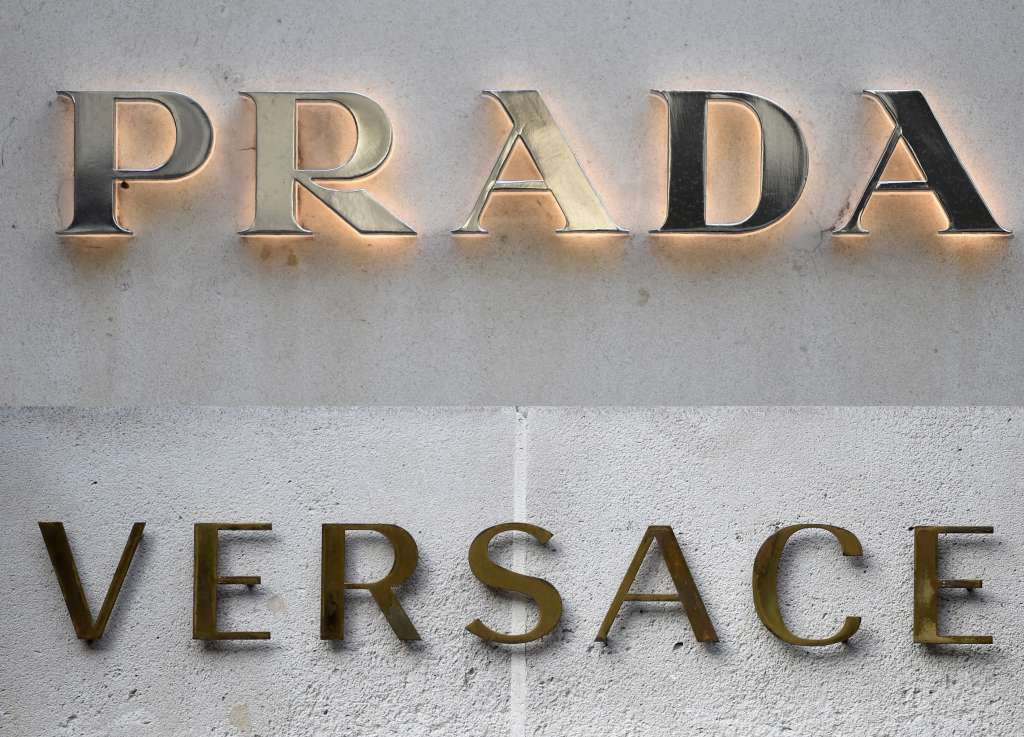 (COMBO) This combination of pictures created on April 10, 2025 shows a file picture of a logo outside the fashion house and luxury goods Versace shop on the Avenue Montaigne in Paris. And a file picture taken on December 19, 2017 of the logo outside the fashion house and luxury goods Prada in Paris.