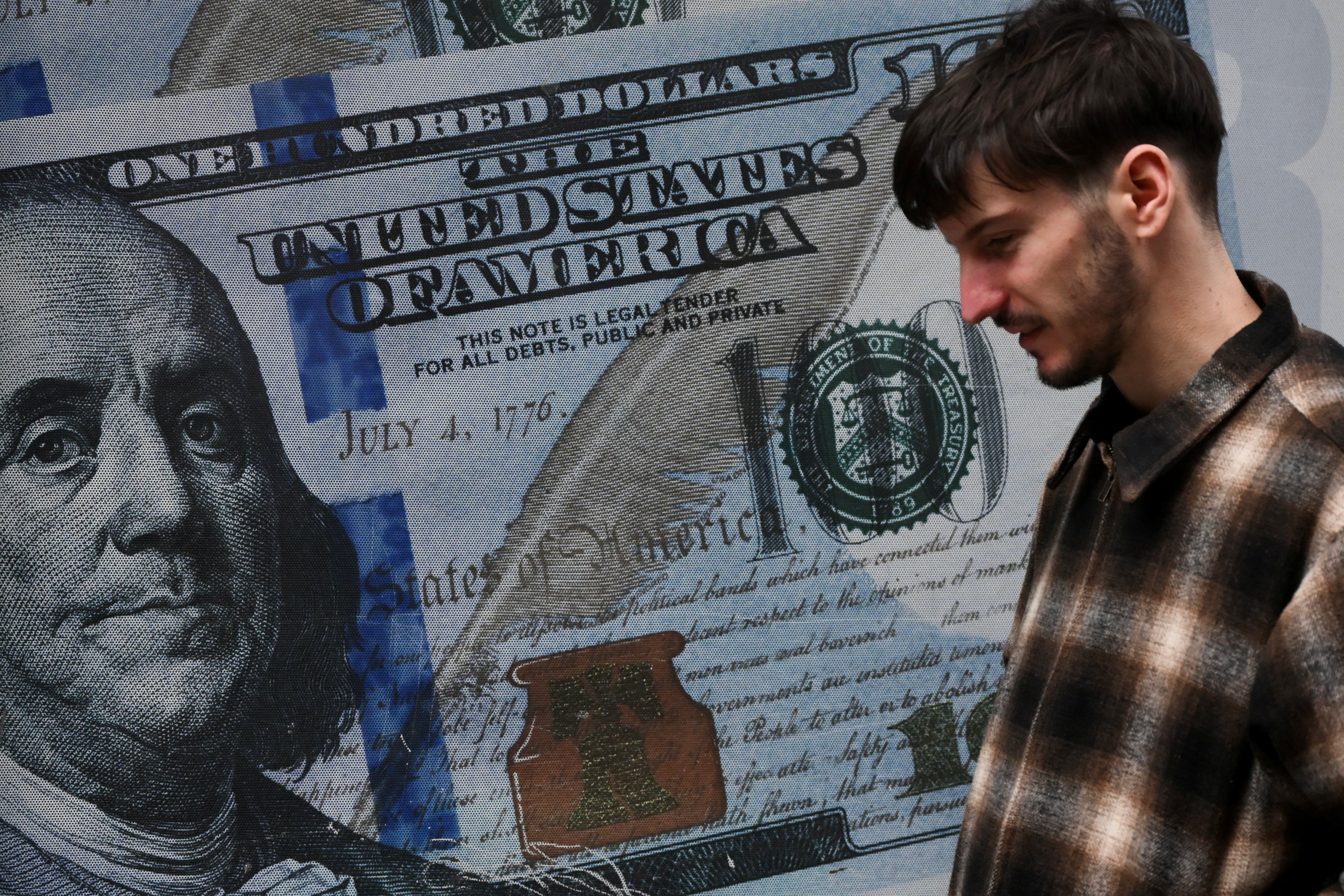 A man walks next to a poster of a giant 100-dollar bill in Buenos Aires, on July 14, 2025. (Photo by Luis ROBAYO / AFP)