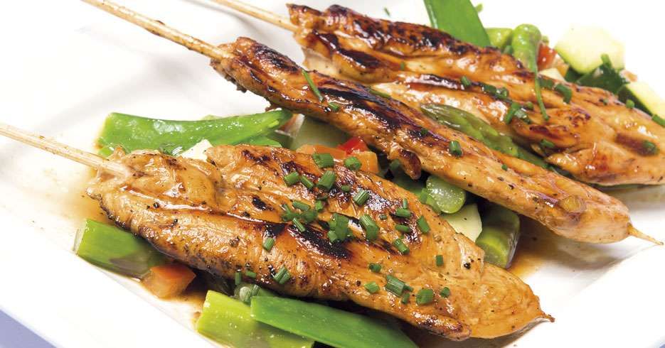 Satays de pollo con salsa barbecue oriental sobre ensalada de pepino cohombro, guisantes y espárragos