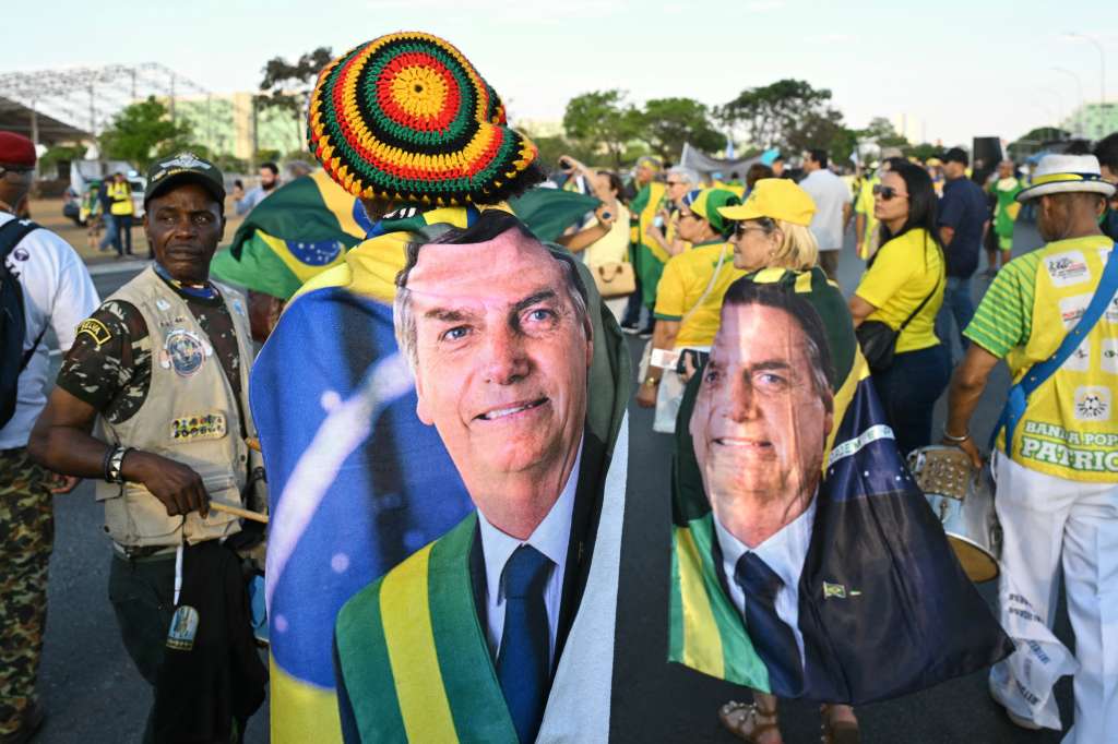 TOPSHOT - Supporters of former Brazilian President Jair Bolsonaro wrapped in flags bearing his image take part in a march calling for amnesty for those convicted of attempting a coup d'état in Brasilia on October 7, 2025. (Photo by Evaristo Sa / AFP)