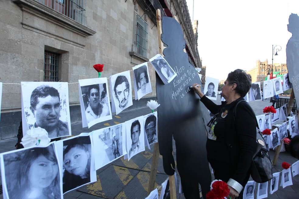 Una mujer escribe en una silueta junto a fotografías de personas desaparecidas este viernes, en las afueras del Palacio Nacional, en Ciudad de México (México). / EFE