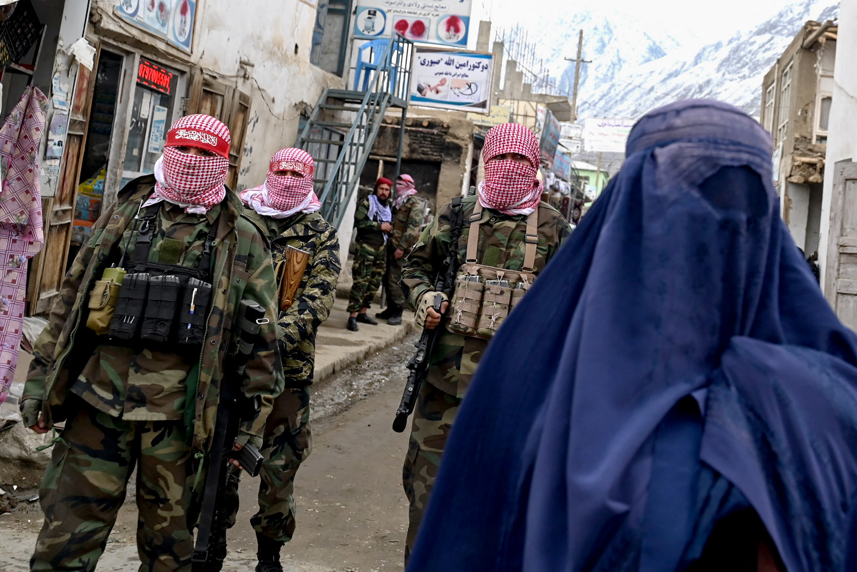 (FILES) Taliban security personnel stand guard as an Afghan burqa-clad woman (R) walks along a street at a market in the Baharak district of Badakhshan province on February 26, 2024.