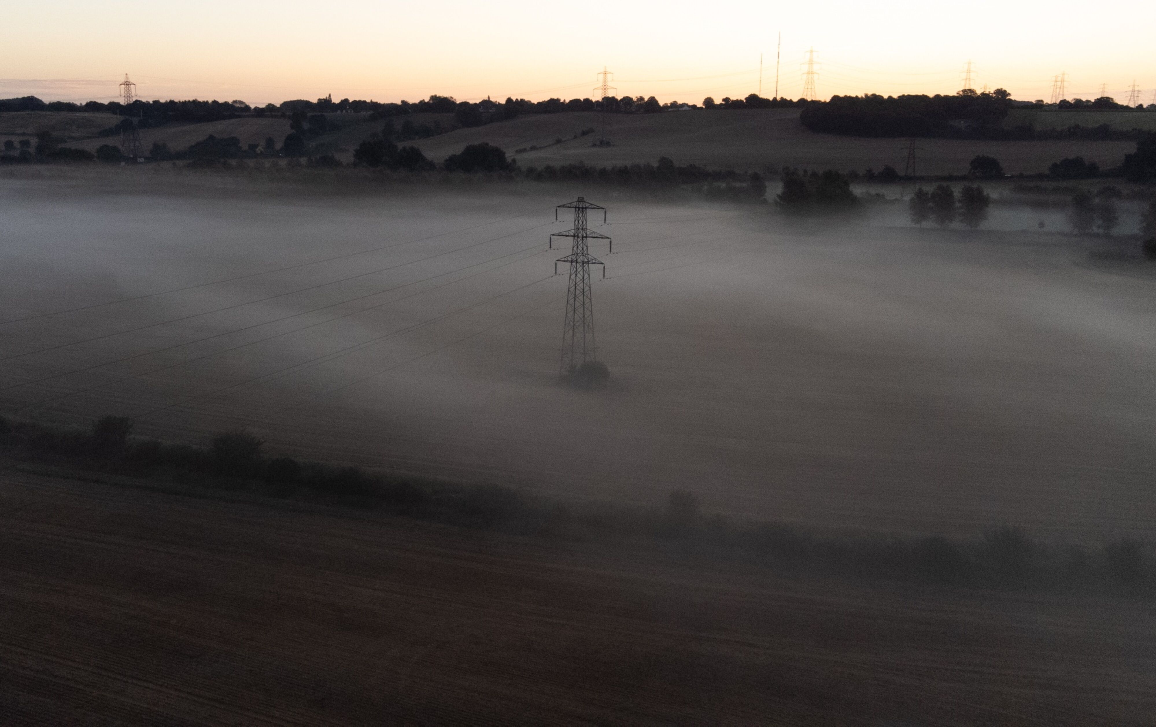Imagen de una torre de electricidad en medio de un paraje cubierto por niebla.