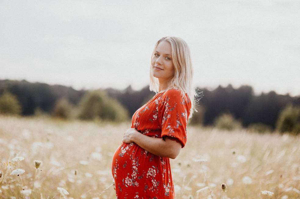 Mujer rubia embarazada con vestido rojo en una pradera.