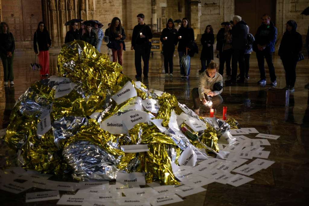 VALENCIA, 29/10/2025.- Varias personas colocan velas en un altar improvisado en el acto de denuncia y homenaje a las víctimas de la dana en el que 229 mantas térmicas tapizan la plaza de la Virgen en memoria de los que perdieron la vida en la tragedia, este miércoles en Valencia. EFE/ Biel Alino