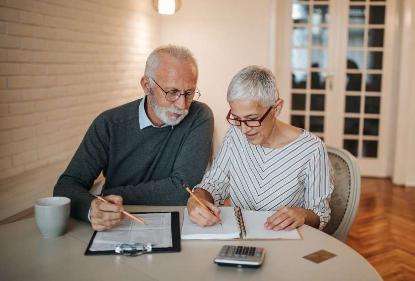 Dos adultos mayores trabajan sentados con unos documentos.