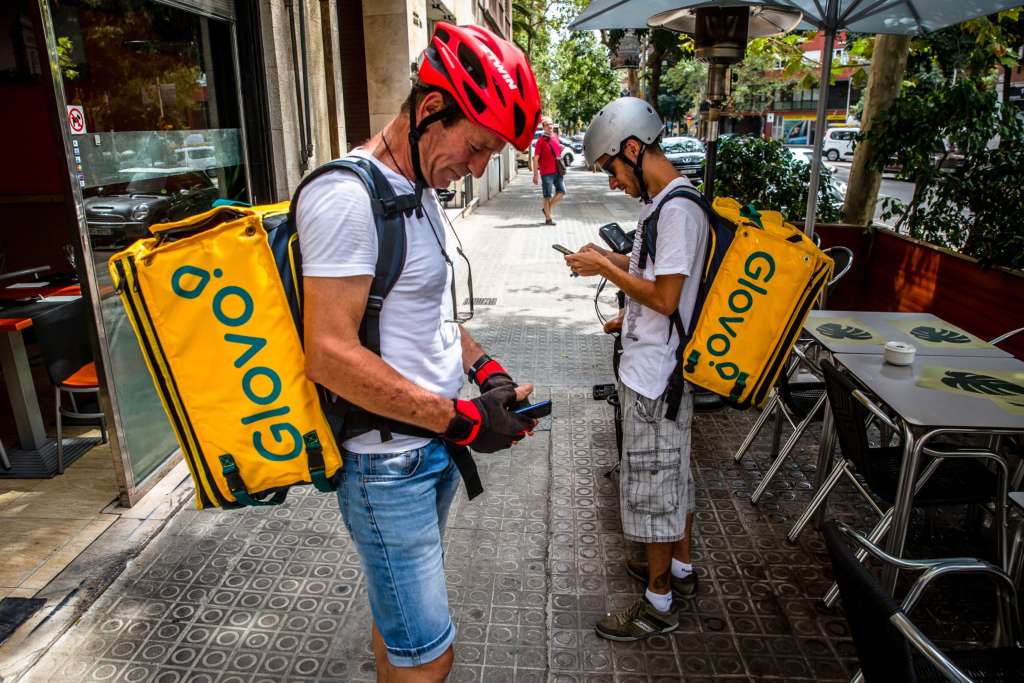 Mensajeros con ropa deportiva y casco sostienen celulares con las manos.