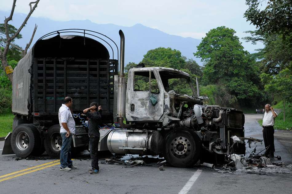 Varios hombres junto a una tractomula incinerada en el Alto de Boquerón (Tolima), durante el paro cafetero.