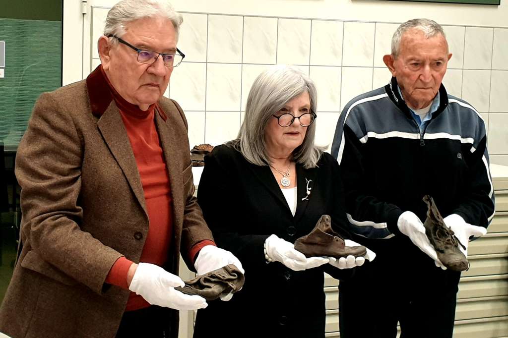AUSCHWITZ, 22/09/2022.- (De i a): Bogdan Barnikowski, superviviente de Auschwitz, Phylis Greenberg Heideman, presidenta de la organización Marcha de los Vivos, y Arie Pinsker, superviviente de Auschwitz, posan con zapatos que pertenecieron a niños asesinados en el campo nazi de Auschwitz durante la segunda guerra mundial y que van a ser conservados en el museo.-EFE/Miguel Ángel Gayo Macías