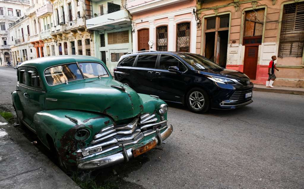 A modern car passes by an old American car parked on a Havana street on September 4, 2024.
