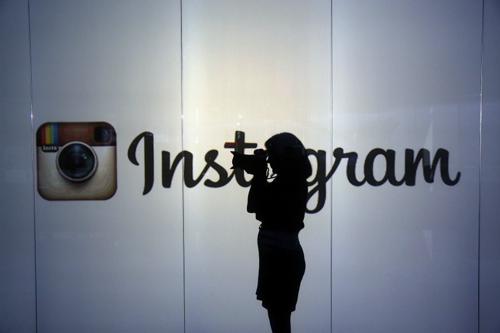Una mujer toma una fotografía con una cámara réflex digital mientras está de pie frente a una pared iluminada que tiene el logotipo de Instagram Inc. en esta fotografía arreglada en Londres, Reino Unido, el martes 5 de enero de 2016.
