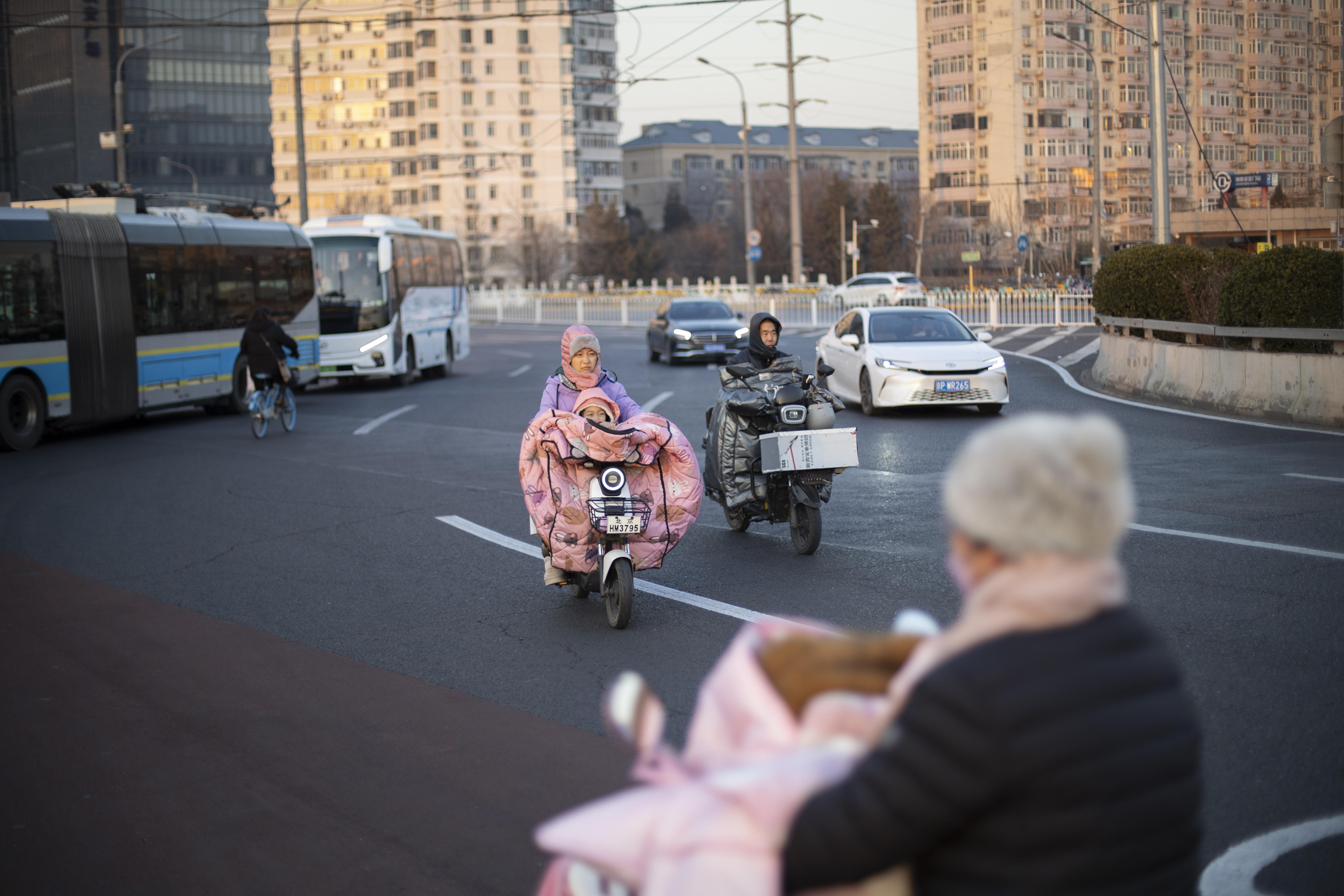 Beijing (China), 17/01/2025.- A woman drives an electric moped carrying a child along a road in Beijing, China, 17 January 2025. The population in China during 2024 decreased by 1.39 million, as the number of newborns was 9.54 million, according to data released by the National Bureau of Statistics today. EFE/EPA/ANDRES MARTINEZ CASARES