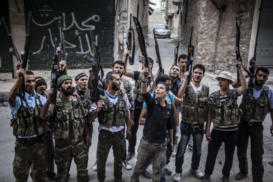 Rebeldes sirios levantan sus armas frente a un edificio recién bombardeado/ EFE