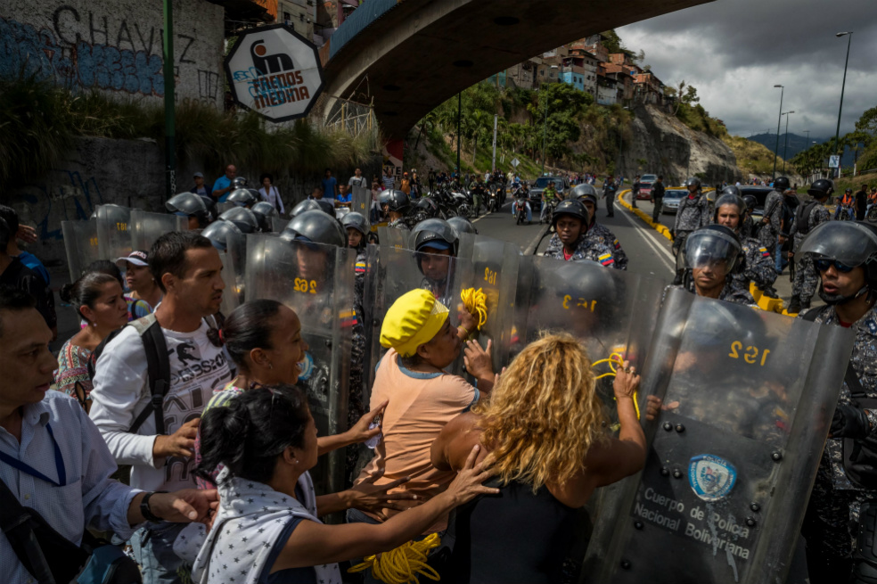 Un grupo de personas protesta frente a miembros de la Policía Nacional Bolivariana por la escasez de alimentos y la falta de gas doméstico y agua. / EFE