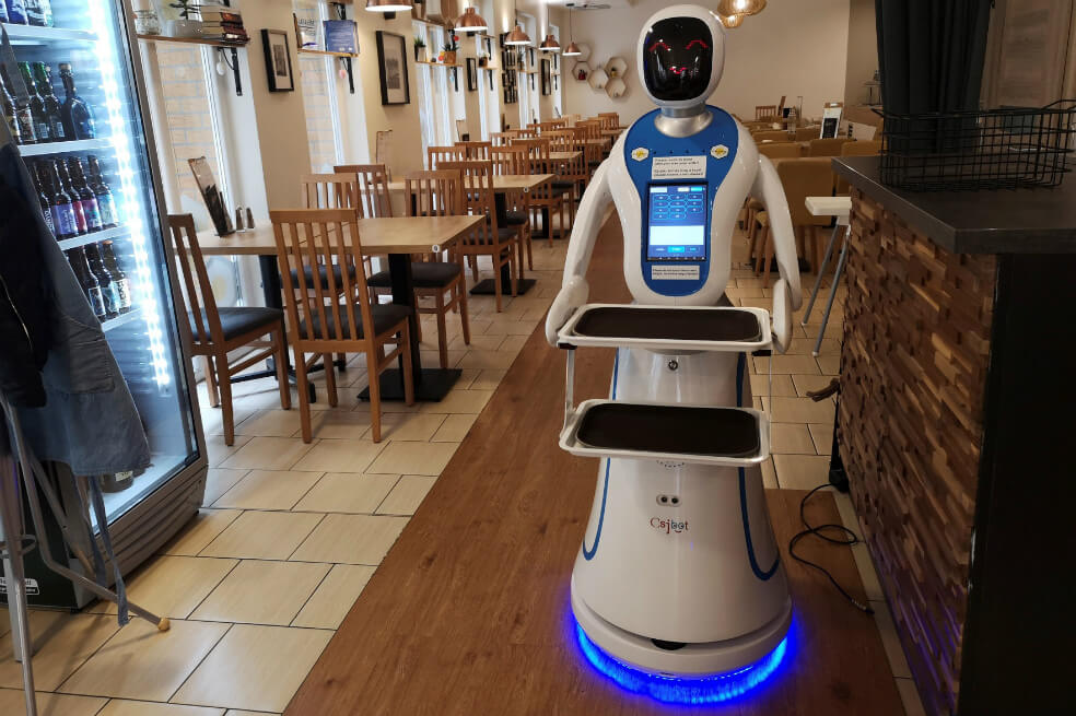 Los robots se mueven en el local en silencio, llevan el café y las comidas a las mesas, donde el cliente se sirve de la bandeja del camarero electrónico, que después de tocarle el "brazo" vuelve hasta el mostrador, para esperar allí al siguiente pedido. / EFE