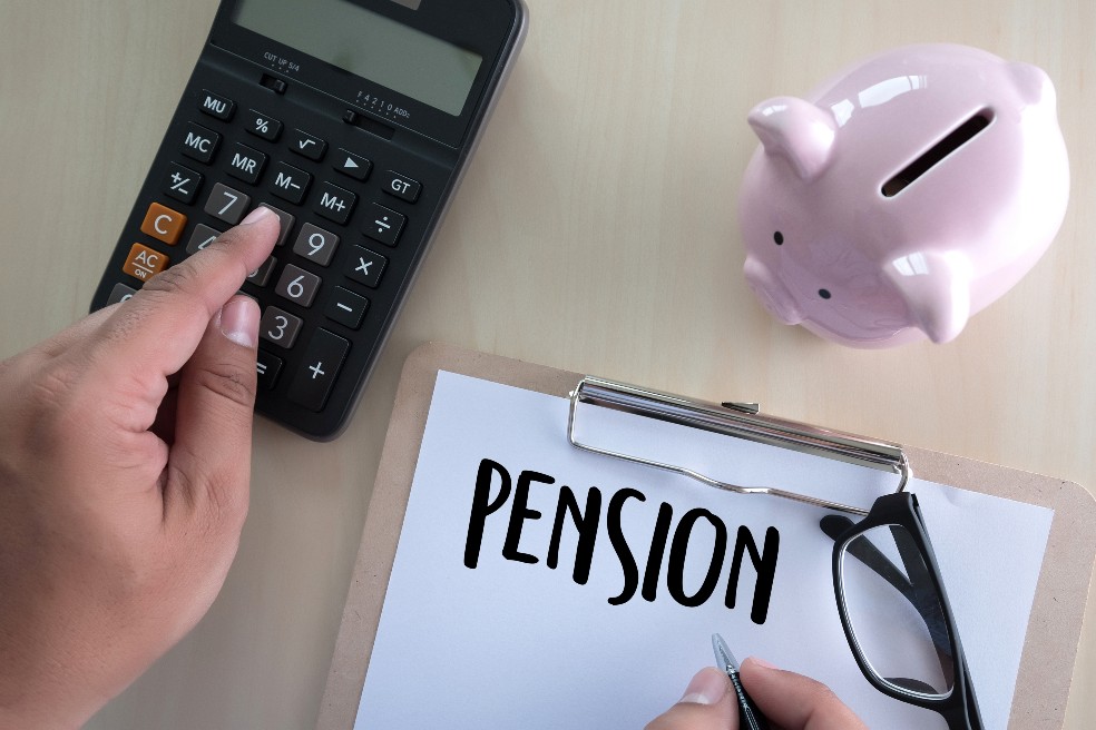 Un tablero con la palabra pensión, una calculadora y un bolígrafo sobre un escritorio.