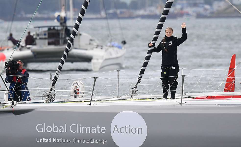 La activista climática sueca Greta Thunberg saluda desde el yate de vela de clase IMOCA Malizia II frente a la costa de Plymouth, suroeste de Inglaterra, este miércoles, mientras comienza su viaje a través del Atlántico hacia Nueva York, donde asistirá a la Cumbre de Acción Climática de la ONU próximo mes. / Ben Stansall / AFP