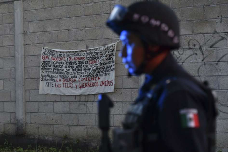 Policía de Iguala junto a un cartel amenazante de la organización criminal Guerreros Unidos.