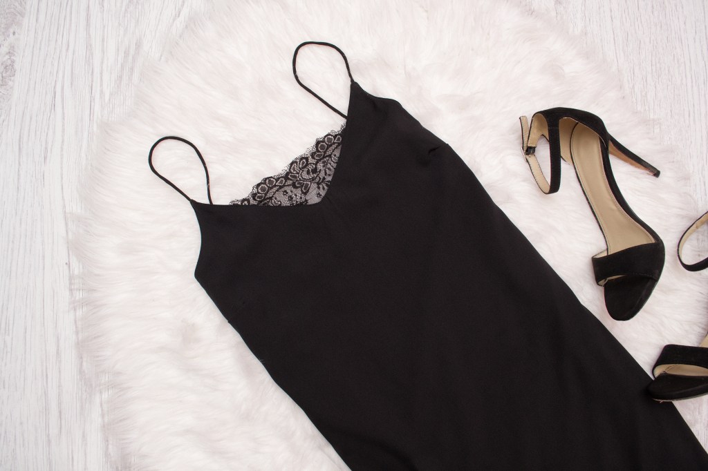 Black simple dress with lace and shoes on white fur, a fashionable concept. Top view