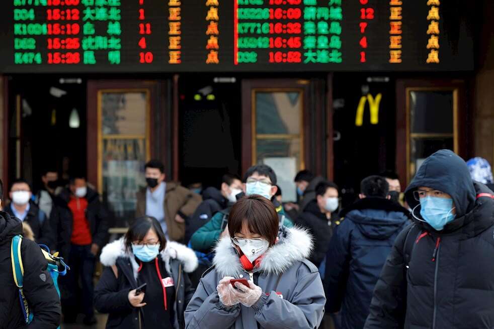 Viajeros se protegen con mascarillas del coronavirus a las puertas de la estación de tren de Pekín, China. / EFE